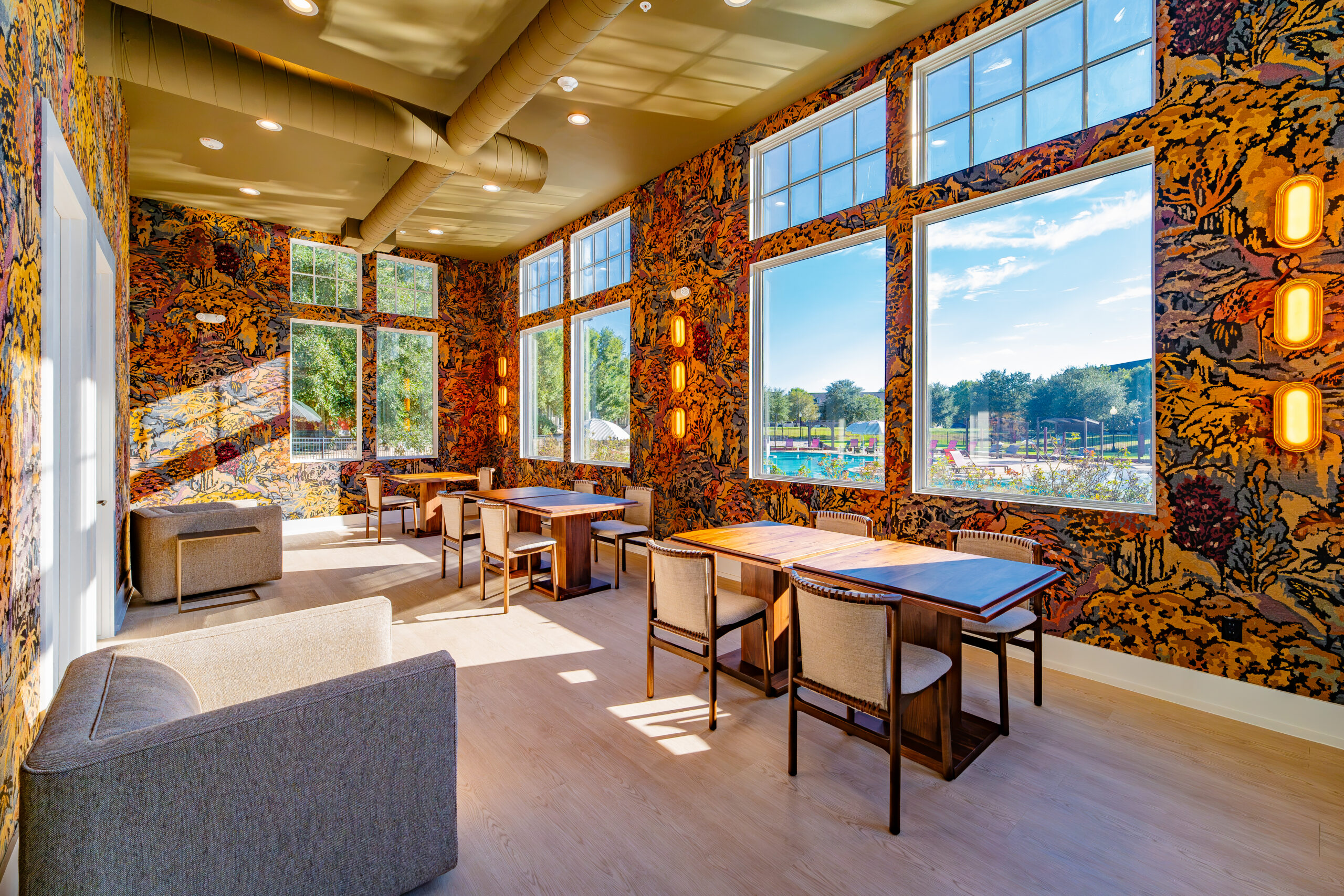 DSC02995 Sunlit community lounge with patterned walls, large windows, tables, and cushioned seating