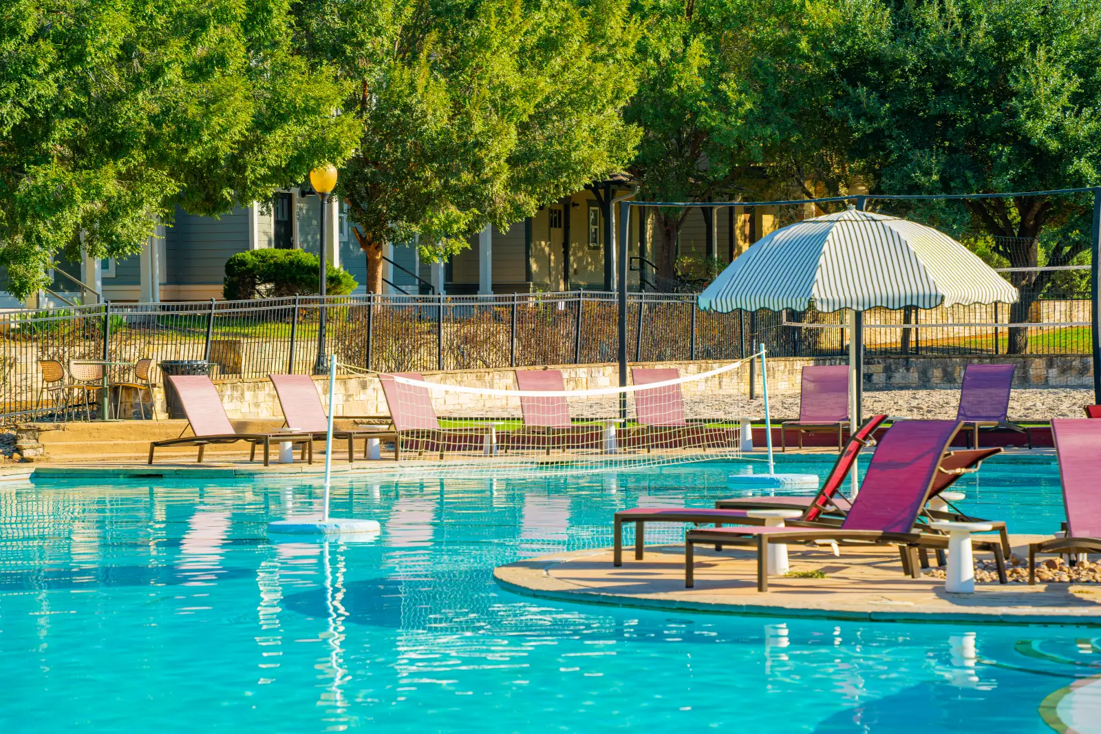 DSC03062 Resort-style swimming pool with purple lounge chairs, striped umbrellas, and surrounding trees